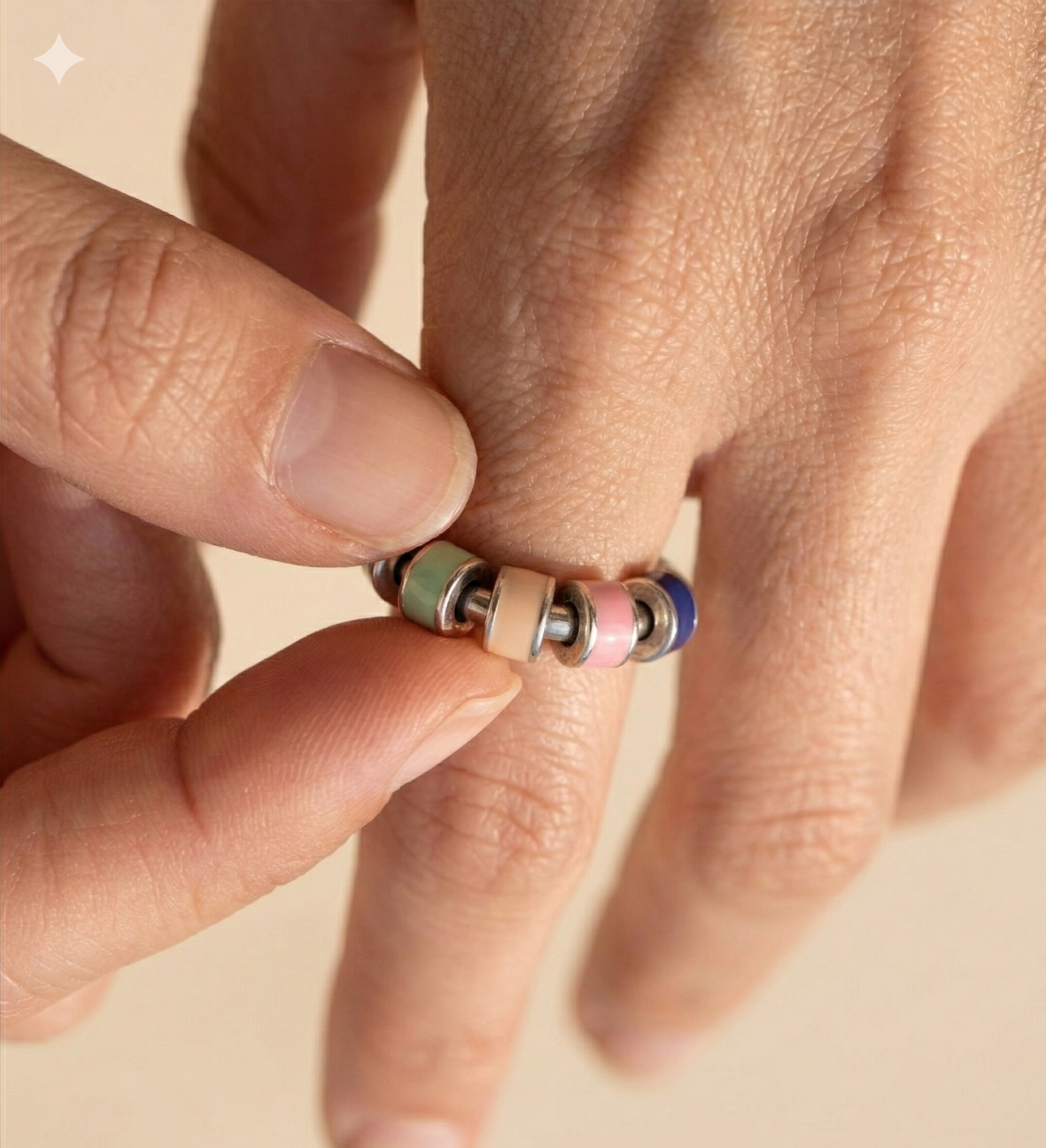 Close-up of a hand wearing a colorful beaded ring on a beige background