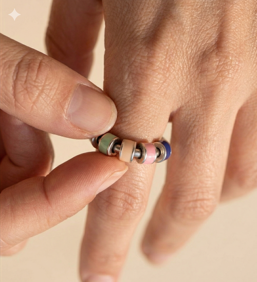Close-up of a hand wearing a colorful beaded ring on a beige background