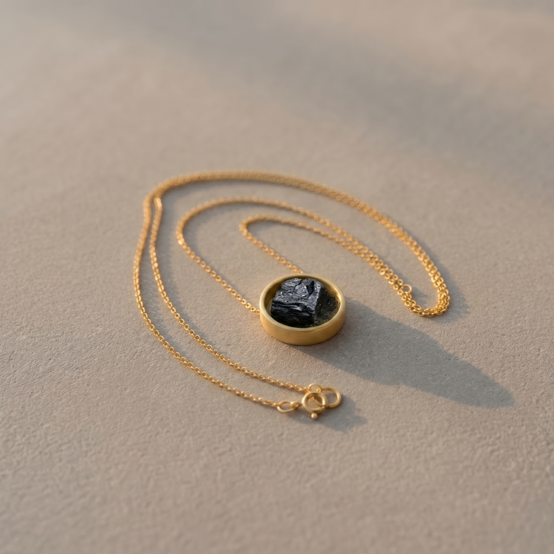 Gold necklace with a black pendant on a beige surface