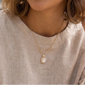 Woman wearing a light-colored shirt and a necklace with a pendant, outdoors.