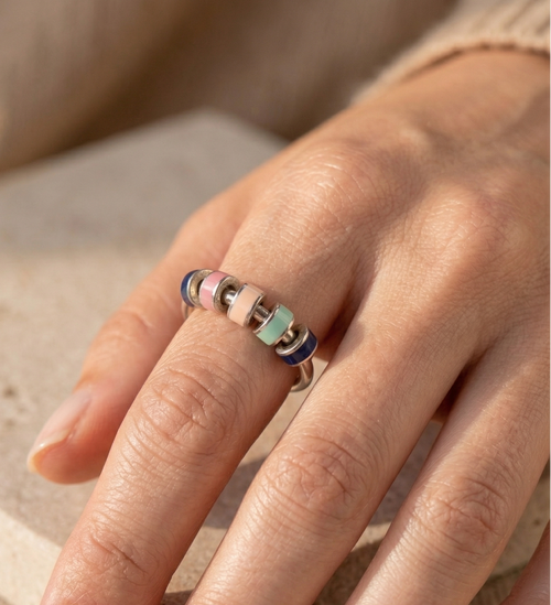 Close-up of a hand wearing a colorful ring on a neutral background