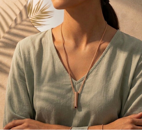 Woman wearing a light green top with a necklace, standing against a neutral background.